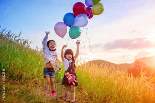 twin kids playing around on the meadow at the hills with holding in hand multicolor ballons