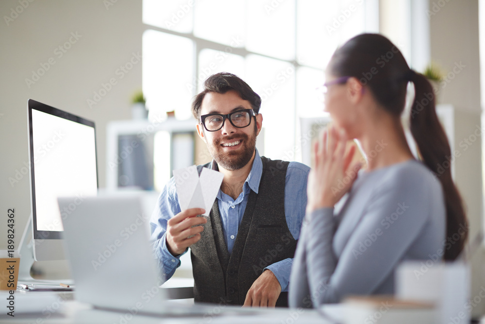 Young businessman inviting his colleague to spend time in theatre after work while showing her two tickets Young businessman inviting his colleague to spend time in theatre after work while showing her two tickets