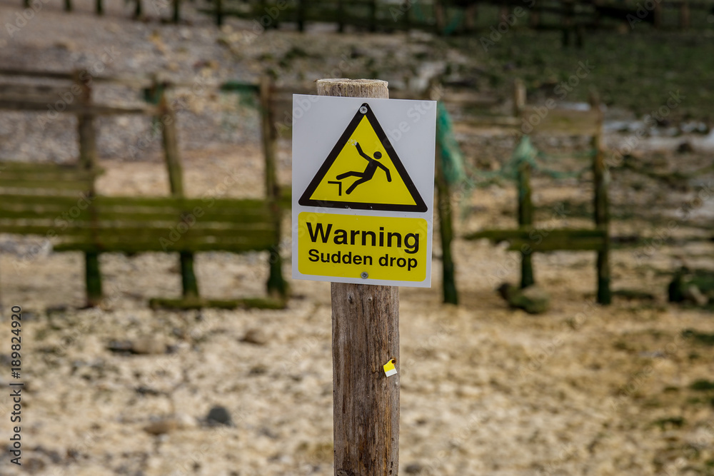 Sign: Warning sudden drop, seen in Cuckmere Haven near Seaford, East Sussex, UK Sign: Warning sudden drop, seen in Cuckmere Haven near Seaford, East Sussex, UK