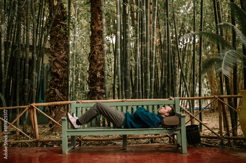 Backpacker man lying on a bench. Man lying on a bench in nature with backpack. Tourist lying on a bench