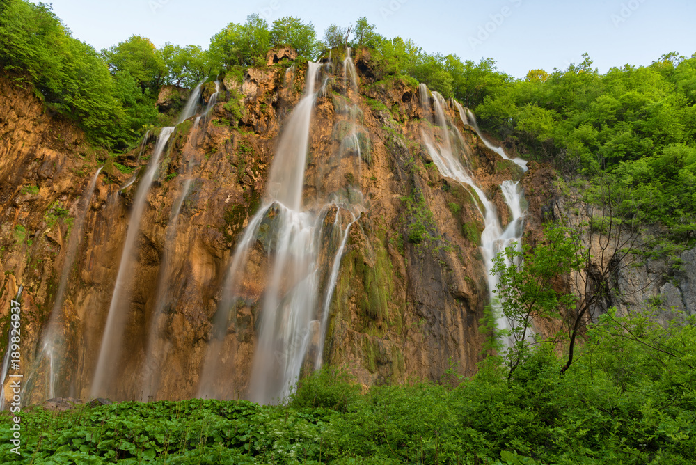 Beautiful view of waterfalls with turquoise water and wooden pathway through over water. Plitvice Lakes National Park, Croatia. Famous attraction, summer landscape.