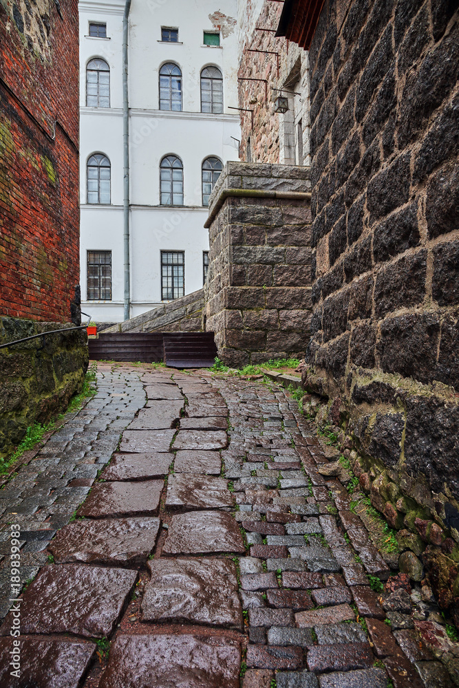 Narrow street in the fortress/Inside the fortress a small short street is paved with cobblestone. On the left and right are stone buildings. Vyborg, Russia, Leningrad region, history