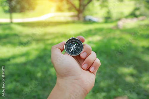 Hand holding a compass against nature background.