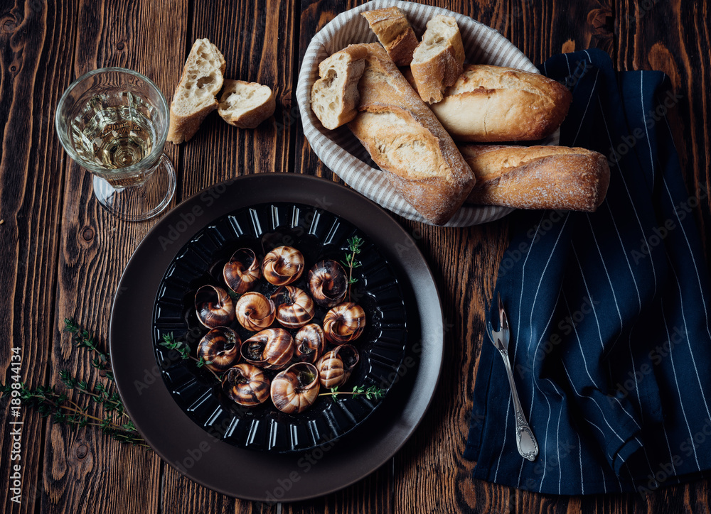 Escargot with glass of white wine and fresh baguette on a dark wooden background.