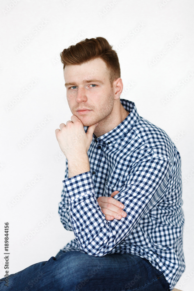 Cheerful handsome redhead young guy in black cardigan checkered shirt photographed against white wall in the studio Cheerful handsome redhead young guy in black cardigan checkered shirt photographed against white wall in the studio