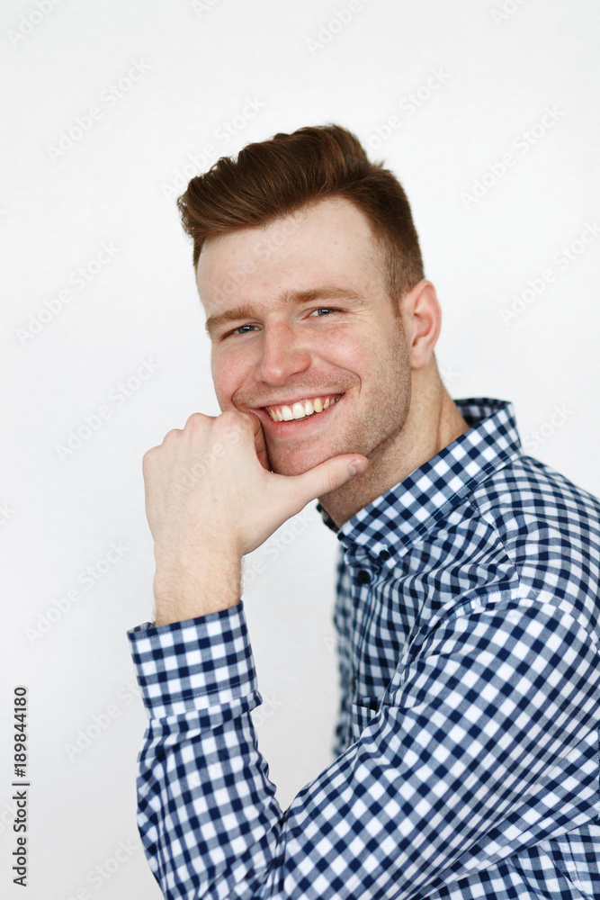 Cheerful handsome redhead young guy in black cardigan checkered shirt photographed against white wall in the studio Cheerful handsome redhead young guy in black cardigan checkered shirt photographed against white wall in the studio