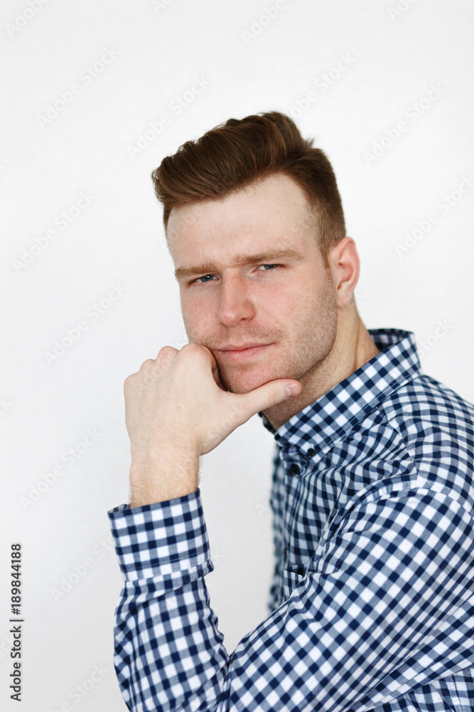 Cheerful handsome redhead young guy in black cardigan checkered shirt photographed against white wall in the studio Cheerful handsome redhead young guy in black cardigan checkered shirt photographed against white wall in the studio