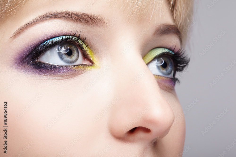 Naklejka premium Closeup macro image of human female eye with violet, blue and and yellow makeup