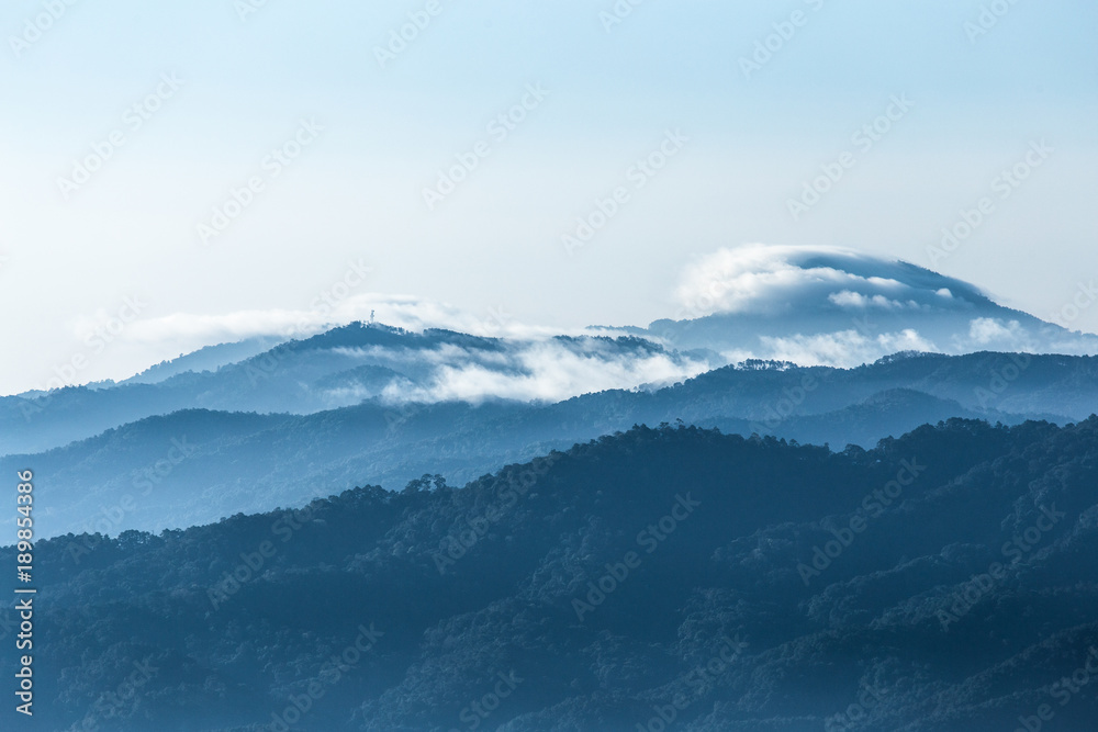 Peak and eadge of blue mountains covered by fog and clouds with bright sky in winter season.