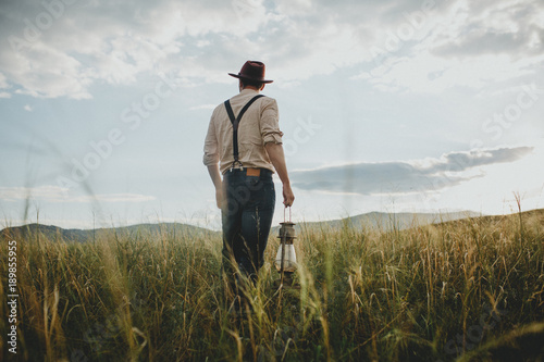 A traveler in retro clothes with an old lamp at sunset outdoors