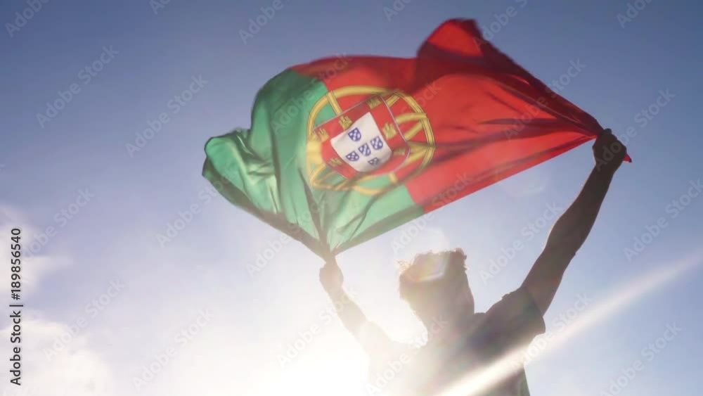 Young man holding portuguese national flag to the sky with two hands at the beach at sunset portugal
