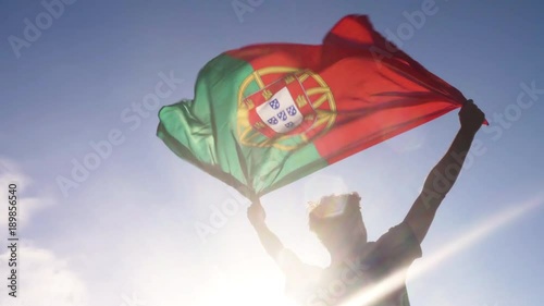 Young man holding portuguese national flag to the sky with two hands at the beach at sunset portugal