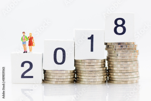 Miniature people : Brother and Sister stand on block 2018 with stack of coins. Image use for business concept.