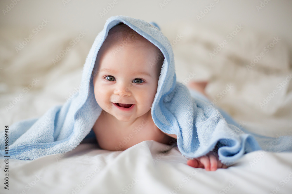 Cute little baby boy, relaxing in bed after bath, smiling happily - obrazy, fototapety, plakaty 