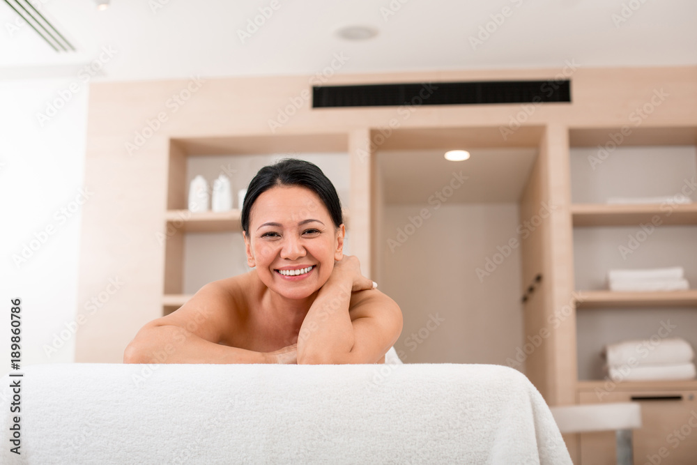 Happy mature woman relaxing after massage session at spa. She is lying on massage table and smiling while looking at camera. Portrait Happy mature woman relaxing after massage session at spa. She is lying on massage table and smiling while looking at camera. Portrait