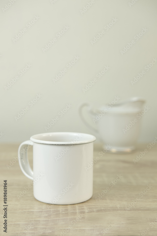 WHITE ENAMEL COFFEE MUG WITH CERAMIC MILK JAR
Enamel white coffee mug with ceramic milk jar on a wood table.