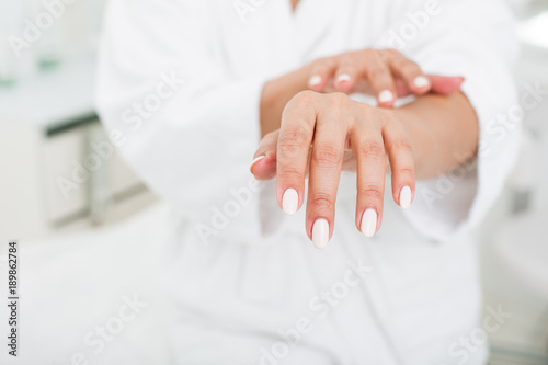 Close up of female hands. Lady putting cream on the skin in beauty salon. Focus on her fingers