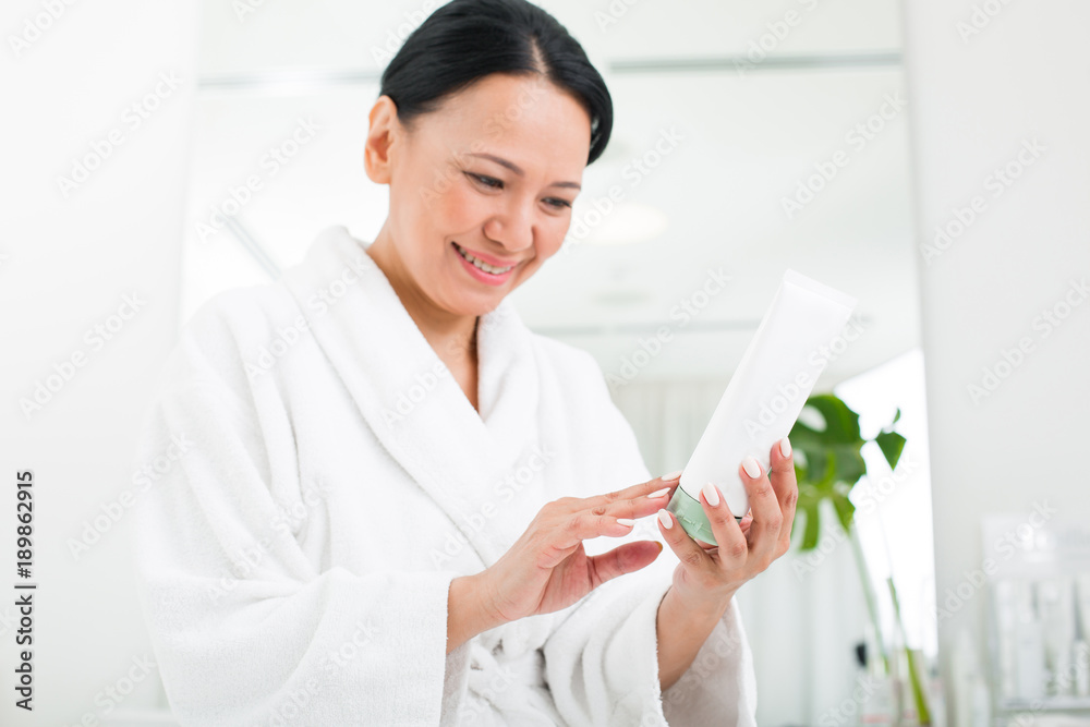 Waist up portrait of serene woman carefully examining the package of cream. She is smiling in wellness center Waist up portrait of serene woman carefully examining the package of cream. She is smiling in wellness center