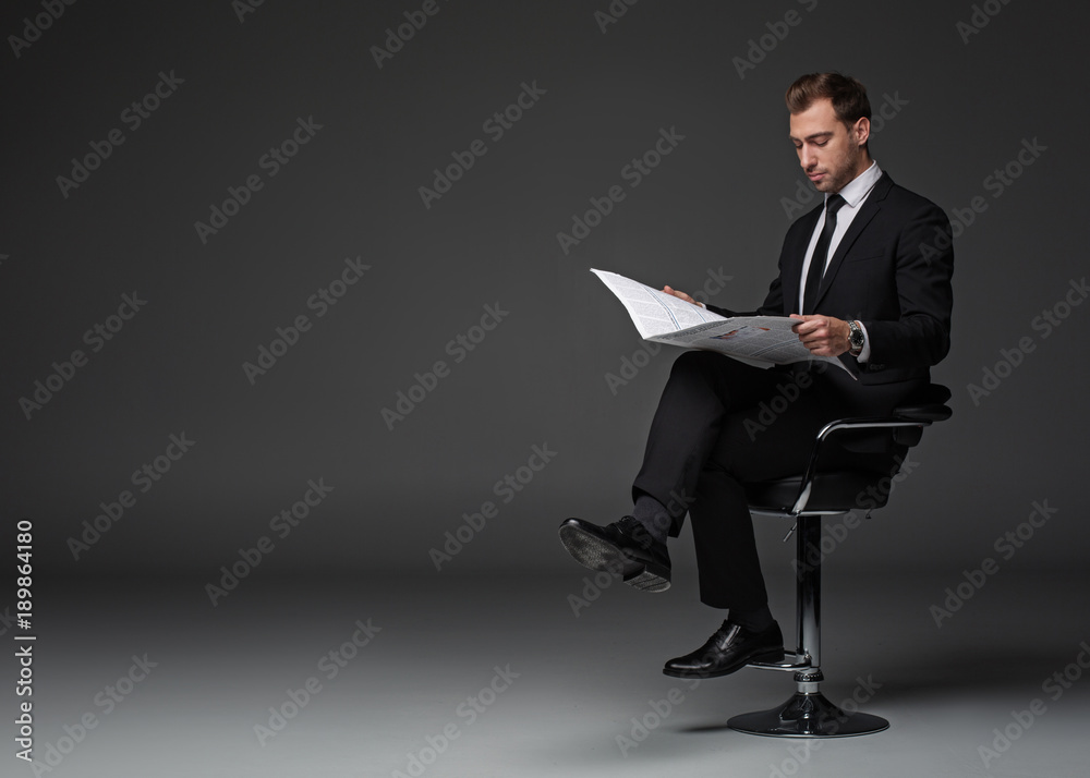 Full length portrait of calm unshaven businessman reading newspaper while sitting on chair. Rest and job concept. Copy space Full length portrait of calm unshaven businessman reading newspaper while sitting on chair. Rest and job concept. Copy space