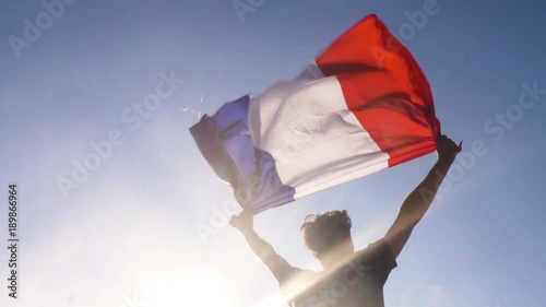 Young man holding french national flag to the sky with two hands at the beach at sunset france