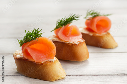 Salmon sandwiches on white wooden board with black olives and herbs.Buffet food, healthy sandwiches
