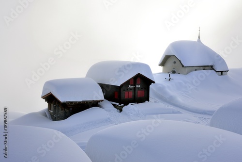 Verschneite Kapelle mit Holzhütten auf Bettmeralp im Nebel