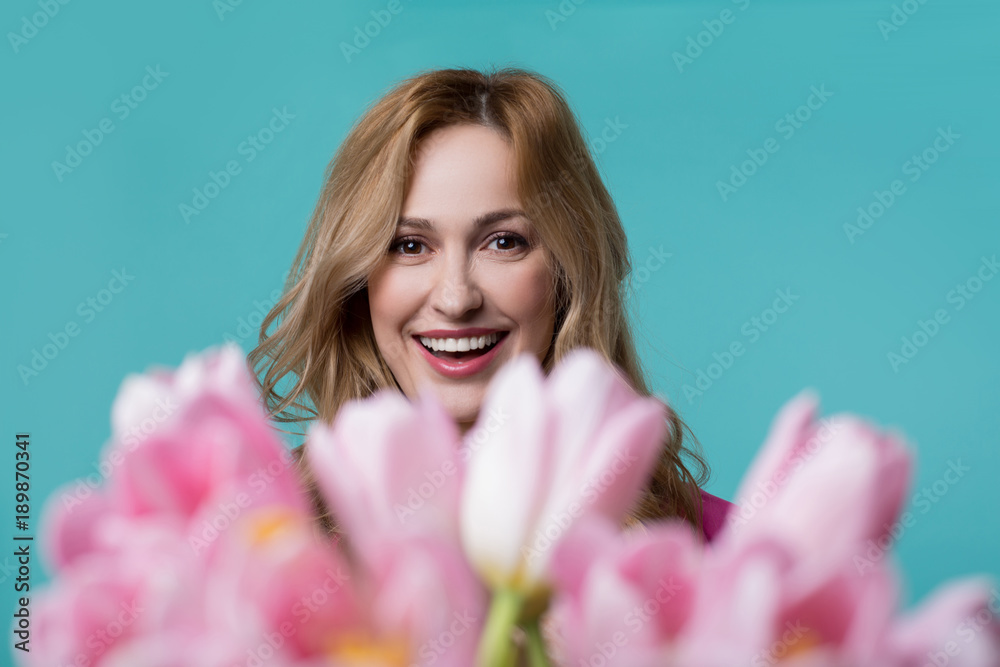 This present is for you. Portrait of cheerful young woman is looking at flowers with amazement. She is standing and smiling. Isolated
