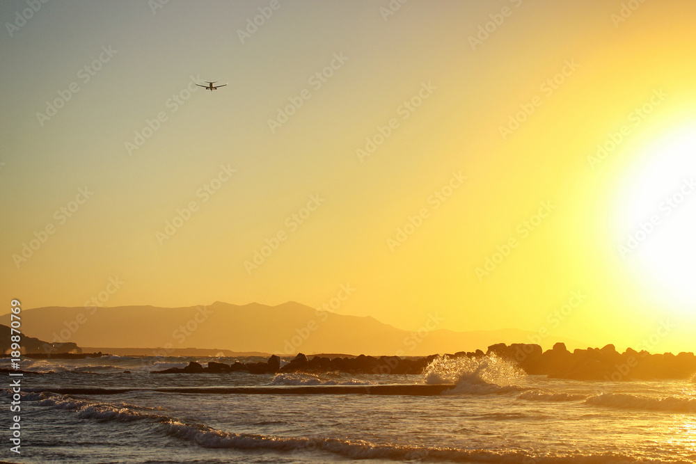 Beautiful orange sunset by the sea in summertime. Plane flying away on the background Beautiful orange sunset by the sea in summertime. Plane flying away on the background