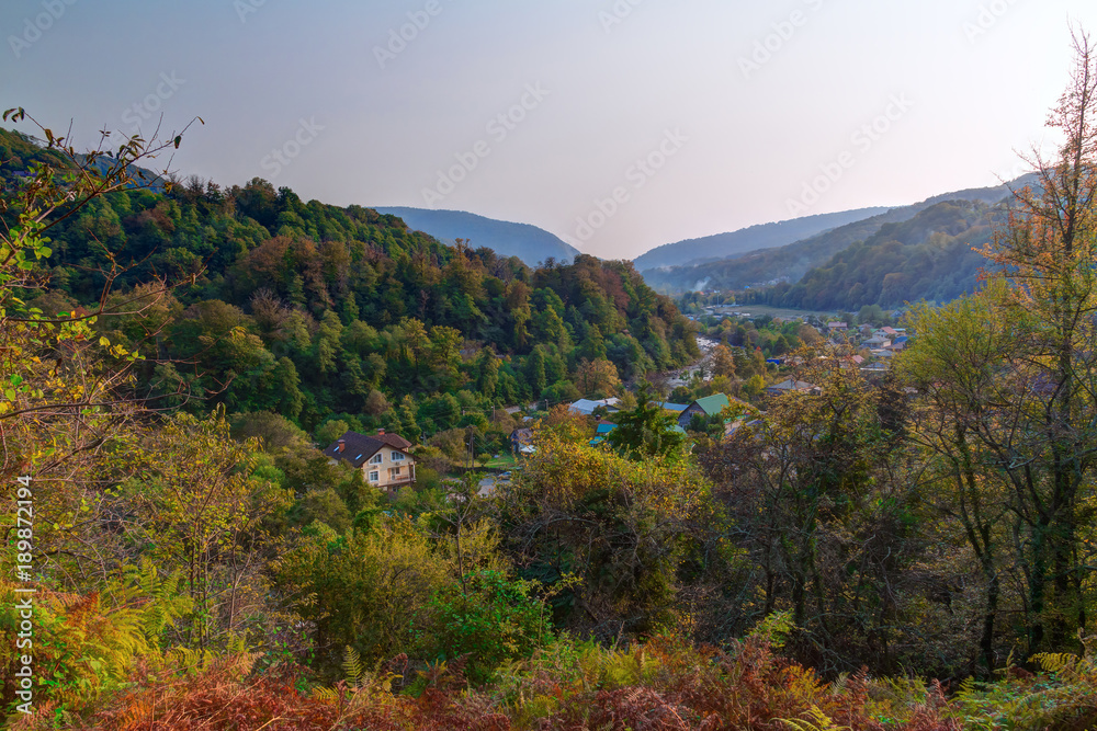 Landscape of Plastunka village in the valley and mountains with varicolored trees in sunny autumn day, Sochi, Russia
