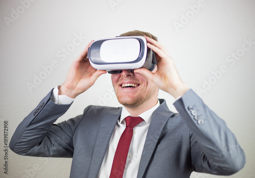 A businessman in a suit, with virtual reality glasses on his eyes, a white background, a delight on his face
