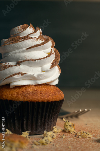 capcake with white cream sprinkled with cocoa on a dark background next to the fork photo