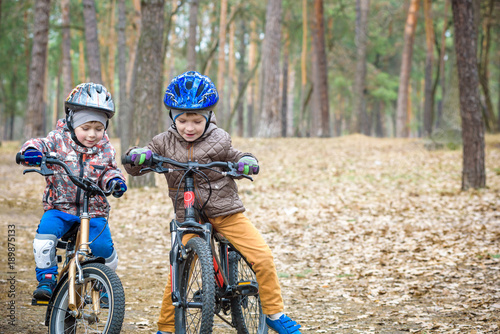 Two little siblings having fun on bikes in autumn or spring forest. Selective focus on boy.