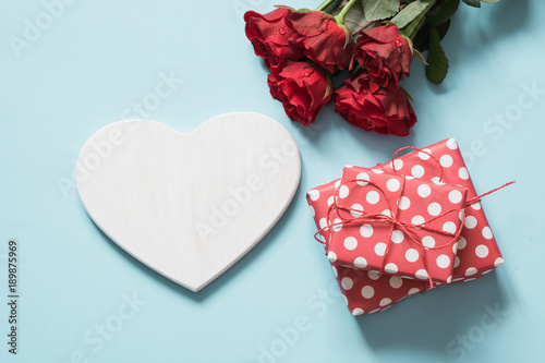 Valentine's day greeting card. Bouquet of red roses and gift, heart as blank for text on blue surface. Copy space.