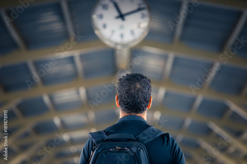 Man with backpack waiting under a clock in a train station