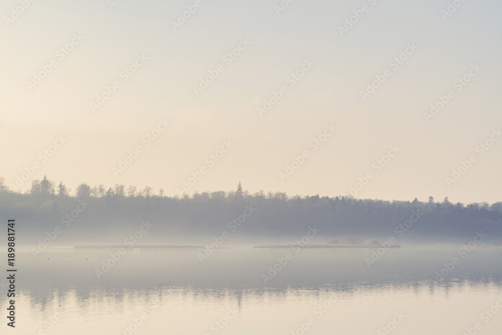 Mist hanging over a quiet lake in the early morning