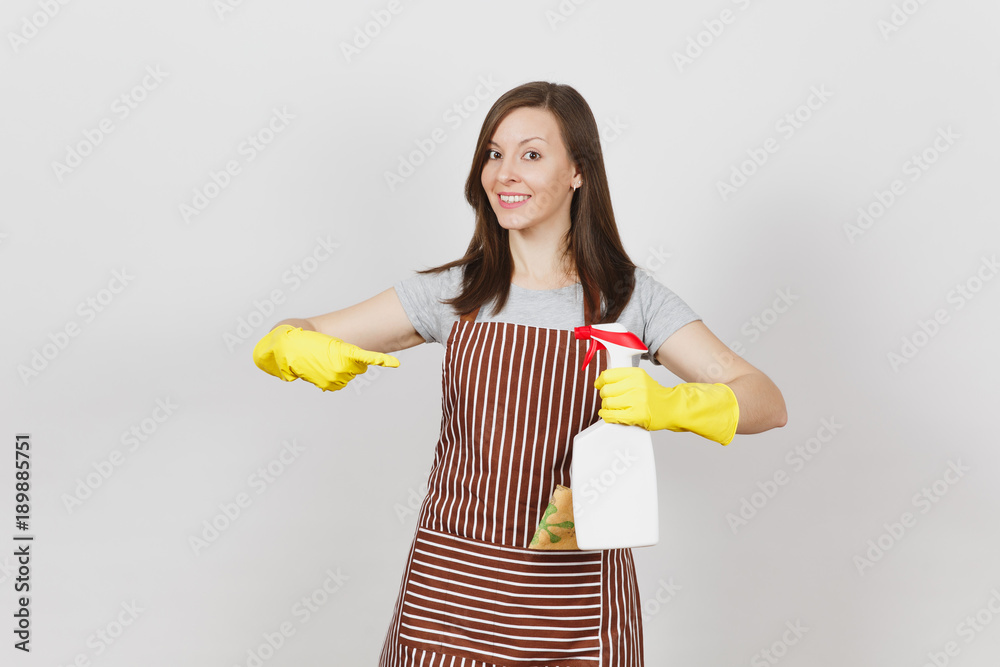 Young housewife in yellow gloves, striped apron, cleaning rag in pocket isolated on white background. Woman holding and pointing on bottle with cleaner liquid, sponge. Copy space for advertisement. Young housewife in yellow gloves, striped apron, cleaning rag in pocket isolated on white background. Woman holding and pointing on bottle with cleaner liquid, sponge. Copy space for advertisement.