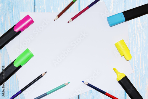 A white sheet of paper lay on a wooden table, near , pencils, markers, pens . The view from the top. photo