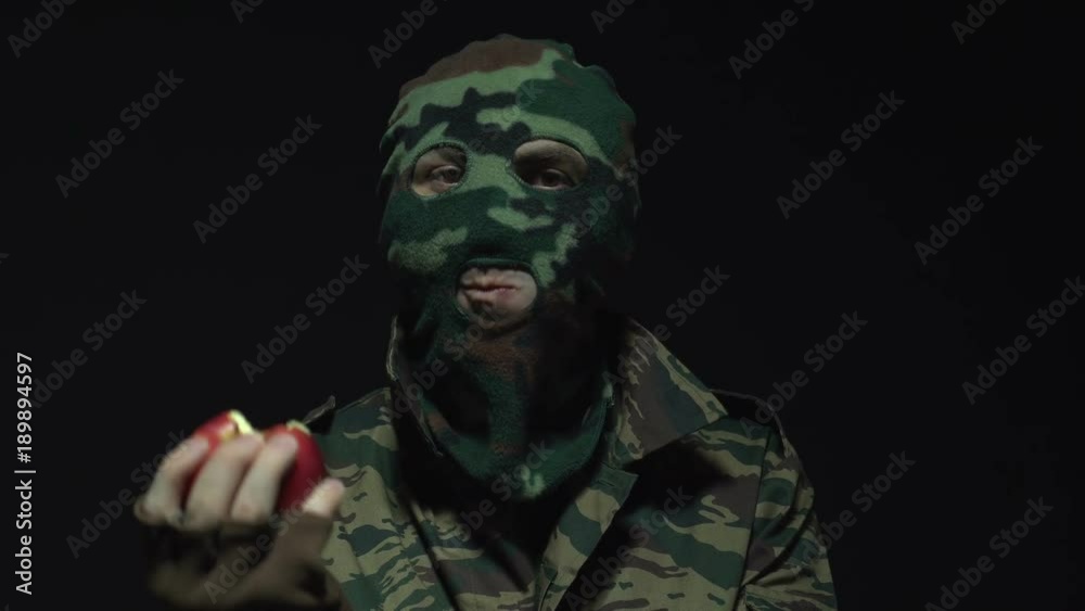 Soldier in camouflage and military mask eating red apple over black background Soldier in camouflage and military mask eating red apple over black background