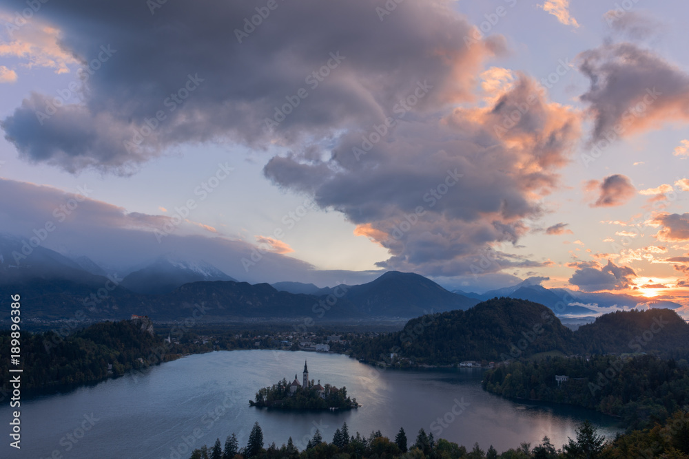 The sun just about to peak out from behind the clouds at Lake Bled. The clouds are blue and orange in color and shows reflecting off the lake.