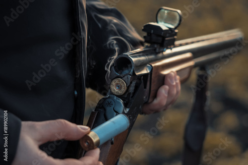 Sports shooting. Hunter reloading cartridge in field. Smoke from the trunks of smooth-bore hunting rifle after firing.