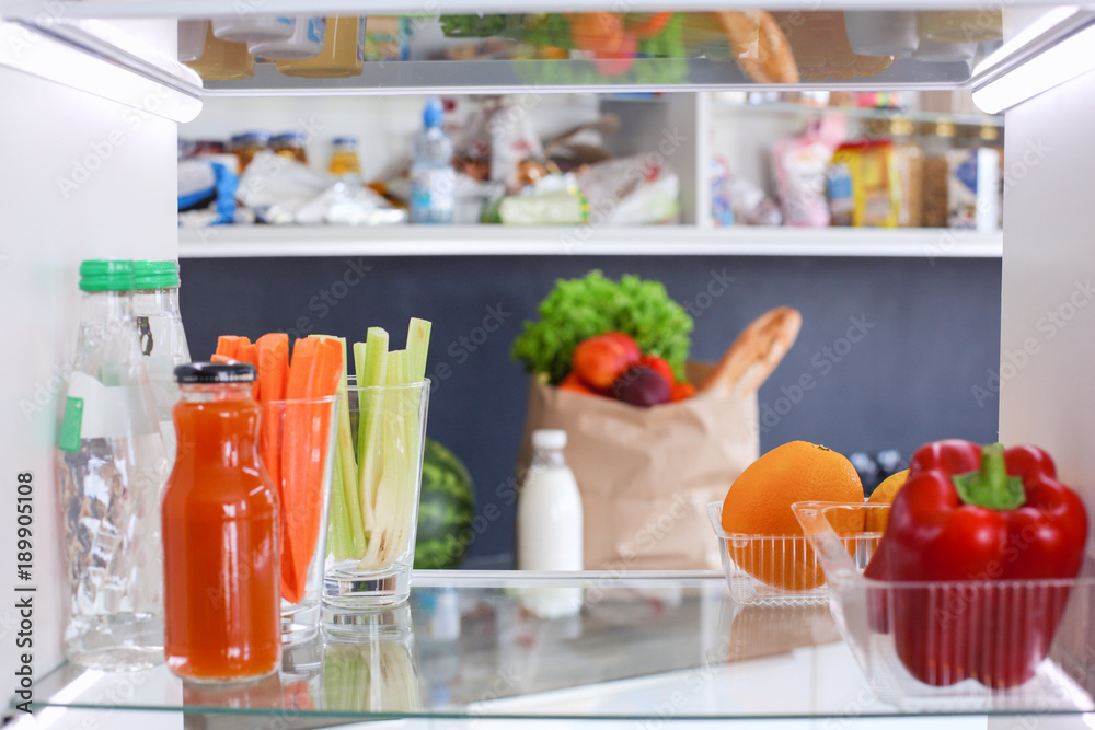 Portrait of female standing near open fridge full of healthy food, vegetables and fruits. Portrait of female