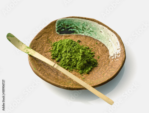 Japanese matcha green tea powder on a ceramic clay plate with a chasaku bamboo spoon (used to scoop the maccha in a bowl during tea ceremony) on white background. photo