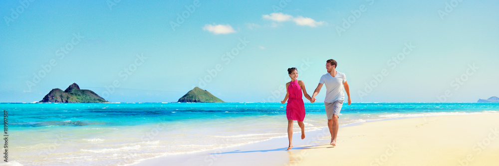 Hawaii vacation couple walking relaxing on white sand and pristine turquoise ocean water on Hawaiian beach Lanikai, Oahu island, USA. Holiday background with blue sky copy space for travel concept.