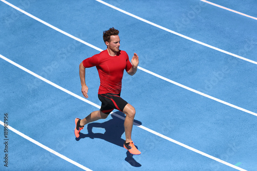 Sprinter man running on blue tracks lanes in track and field stadium in high speed top view. Male athlete runner in intense sprint training. Run sport concept © Maridav