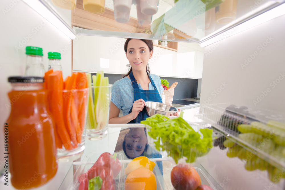 Portrait of female standing near open fridge full of healthy food, vegetables and fruits. Portrait of female Portrait of female standing near open fridge full of healthy food, vegetables and fruits. Portrait of female