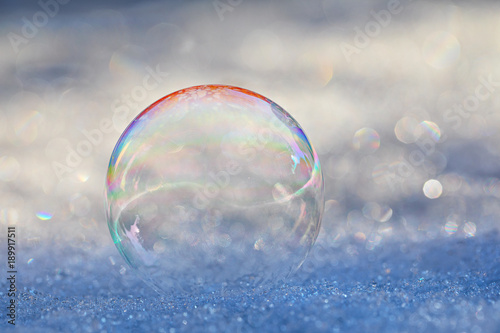 A soap bubble on the snow making a natural yin-yang design with the light, a prism effect, and bokeh from the sun on the snow