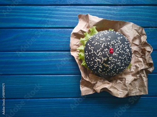 Черный  гамбургер  со шпажкой в виде сердечка на синем деревянном фоне