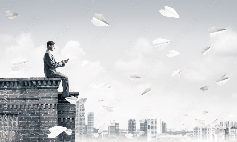 Businessman or student on roof edge making calls and cityscape a Businessman or student on roof edge making calls and cityscape a