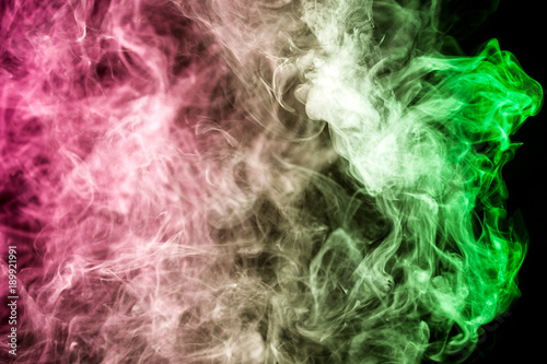Thick colorful smoke of green and pink on a black isolated background. Background from the smoke of vape