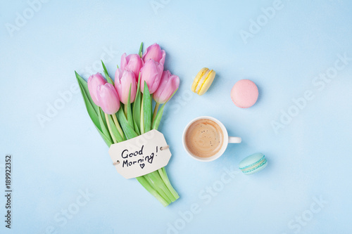 Beautiful breakfast on Mothers or Womans day. Coffee cup with pink tulip flowers  macaroon and note good morning on blue table top view.